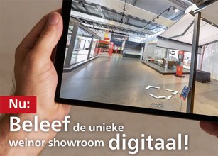 Een hand houdt een tablet met een digitale weergave van een showroom. Achtergrond is neutraal en lichtgrijs.  Een hand houdt een tablet met een digitale weergave van een showroom. Achtergrond is neutraal en lichtgrijs.